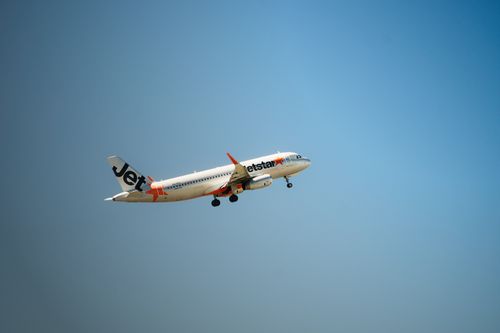 Free Jetstar airplane flying mid-air with clear blue sky backdrop Stock Photo