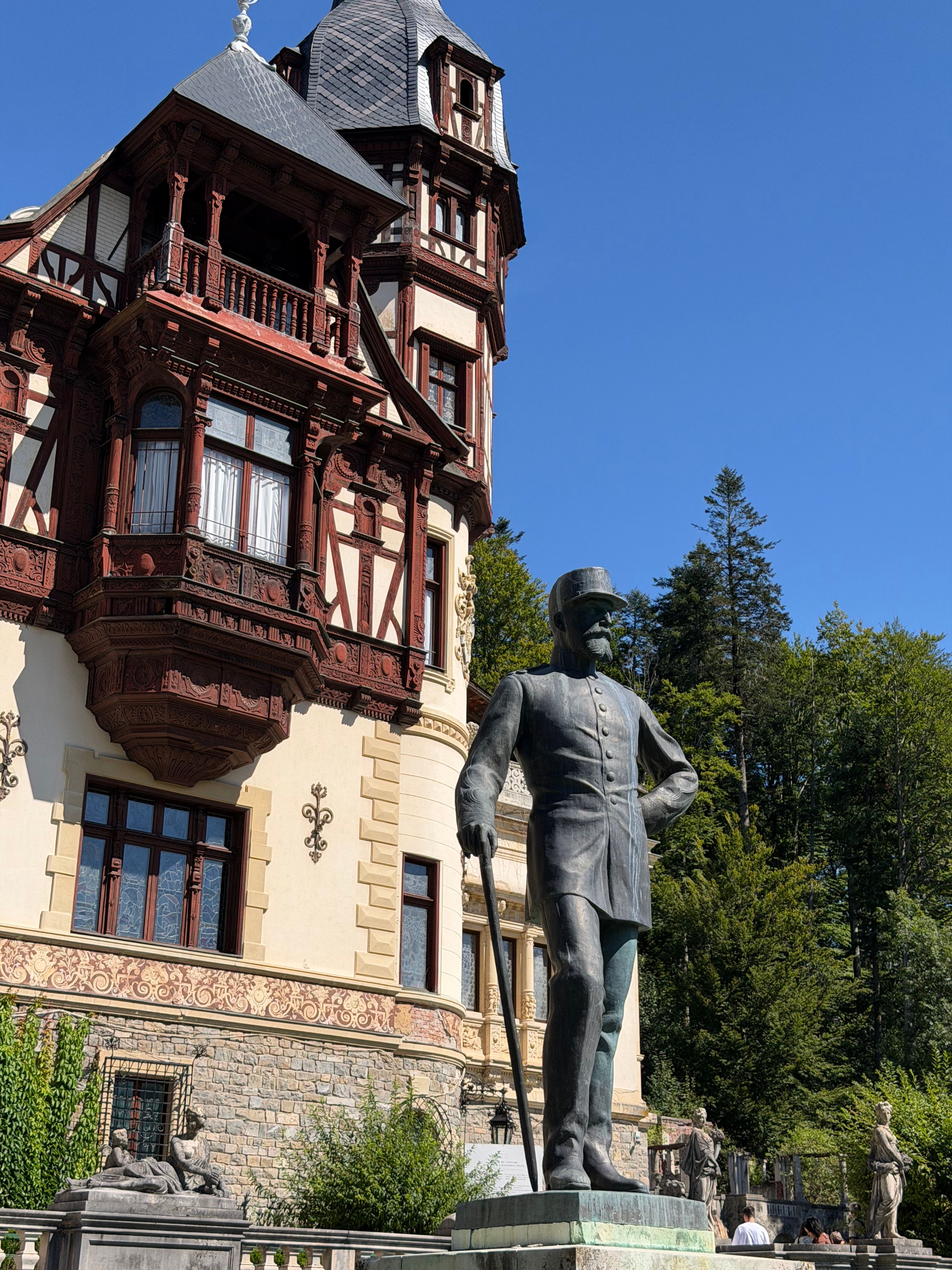 Historic statue view in Sinaia, Romania, with intricate architectural backdrop on a sunny day.