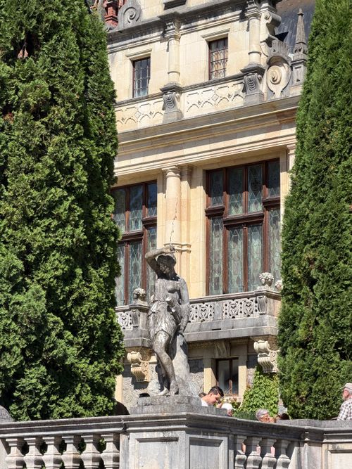 Free A statue stands between tall trees in front of a historic building in Sinaia, Romania. Stock Photo