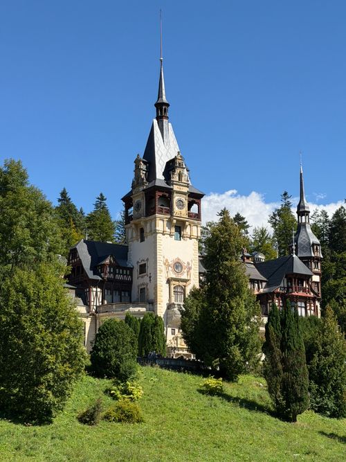 Free Scenic view of Peles Castle surrounded by lush greenery under a clear blue sky in Sinaia, Romania. Stock Photo