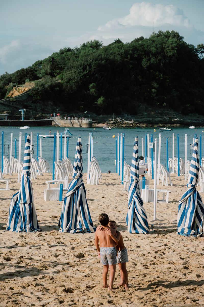Children on La Concha beach in San Sebastián with striped beach tents and Santa Clara Island behind