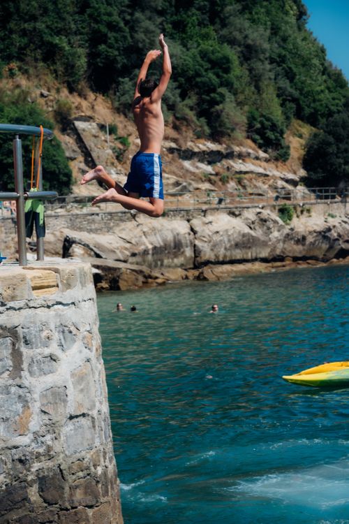 Free A young man in swim trunks jumps off a rocky cliff into the blue sea at San Sebastián, Spain. Stock Photo