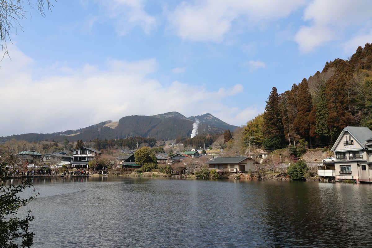 Lakeside houses in Yufuin with forested hills and mountains behind under a clear sky