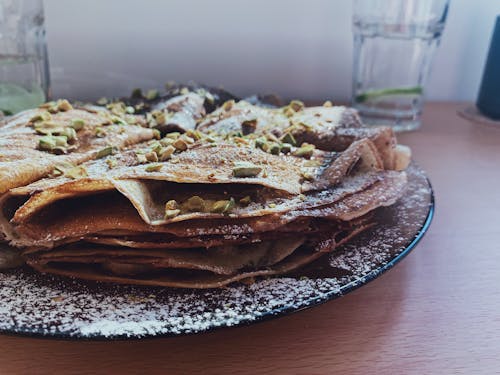 Free Tasty homemade pancakes with garnish placed on black plate near glass of water on wooden table Stock Photo