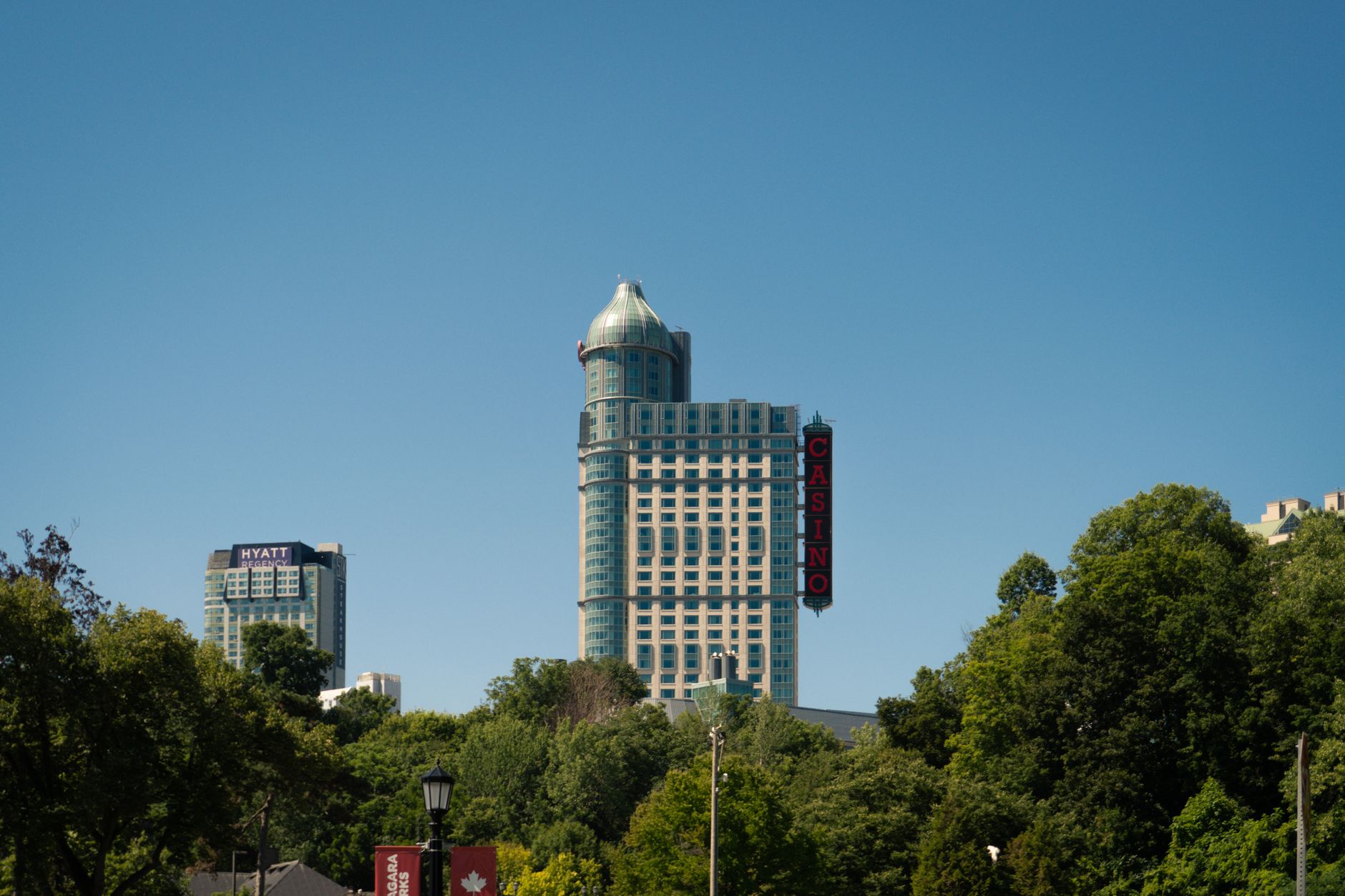 View of Niagara Falls Casino and surrounding hotels surrounded by lush greenery under a clear blue sky.