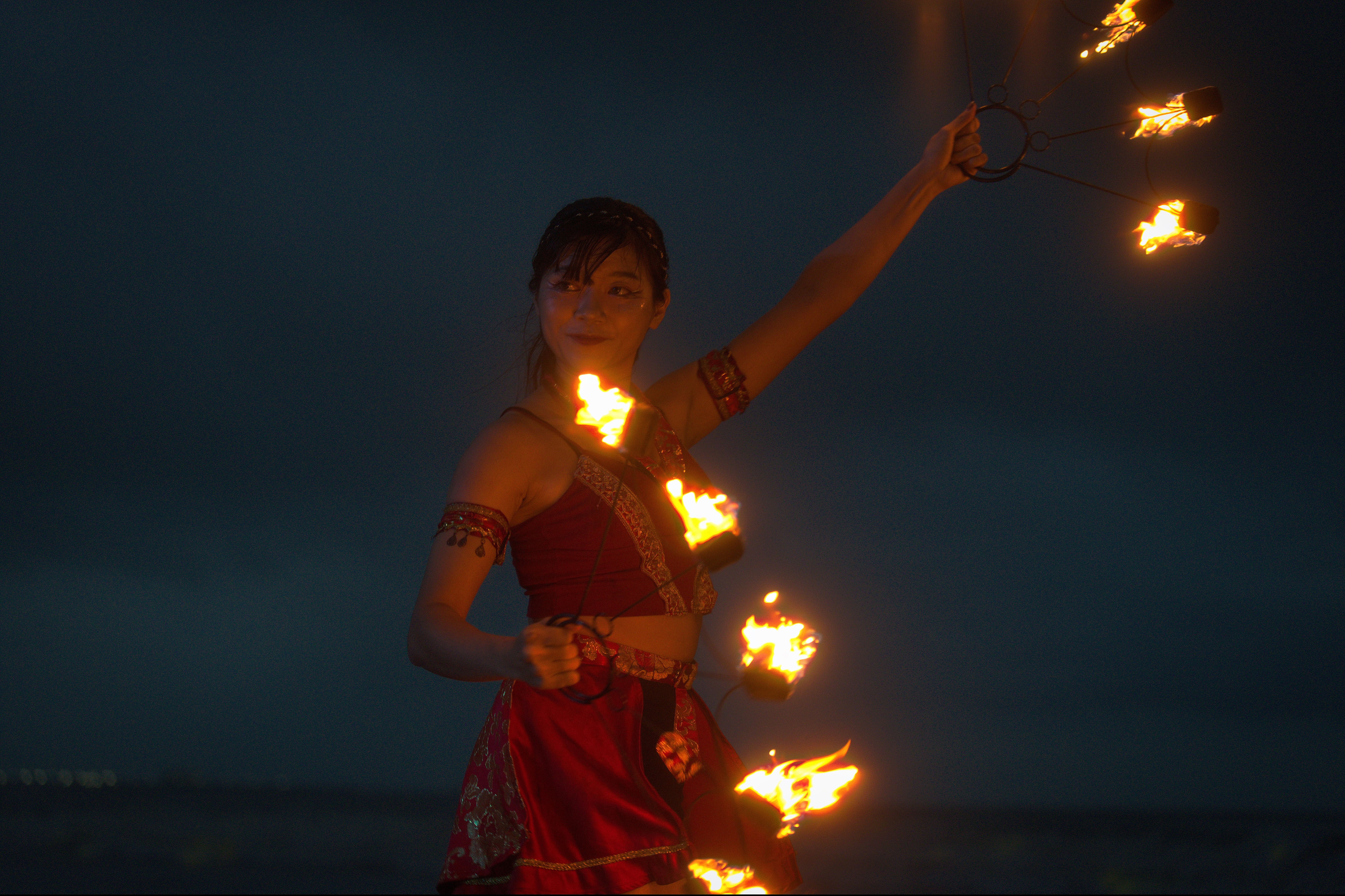 A woman performing fire dance on a beach during nighttime under a dark sky.