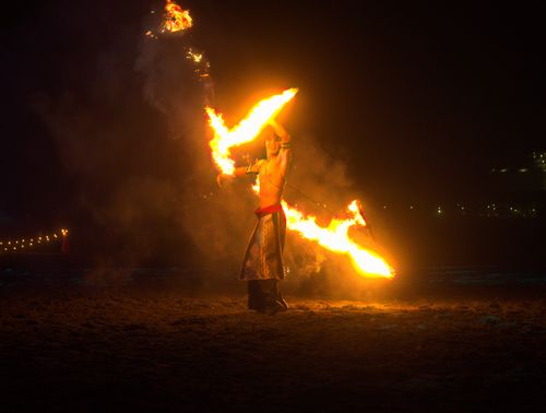 Free A fire performer skillfully handles flames on a beach at night, creating a dramatic visual spectacle. Stock Photo