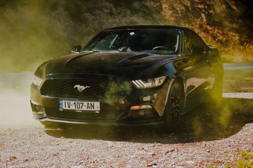 Free Dynamic shot of a black sports car surrounded by yellow dust on a sunny day. Stock Photo
