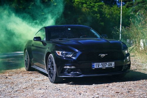 Free A sleek black sports car enveloped in green smoke, parked outdoors on a sunny day. Stock Photo