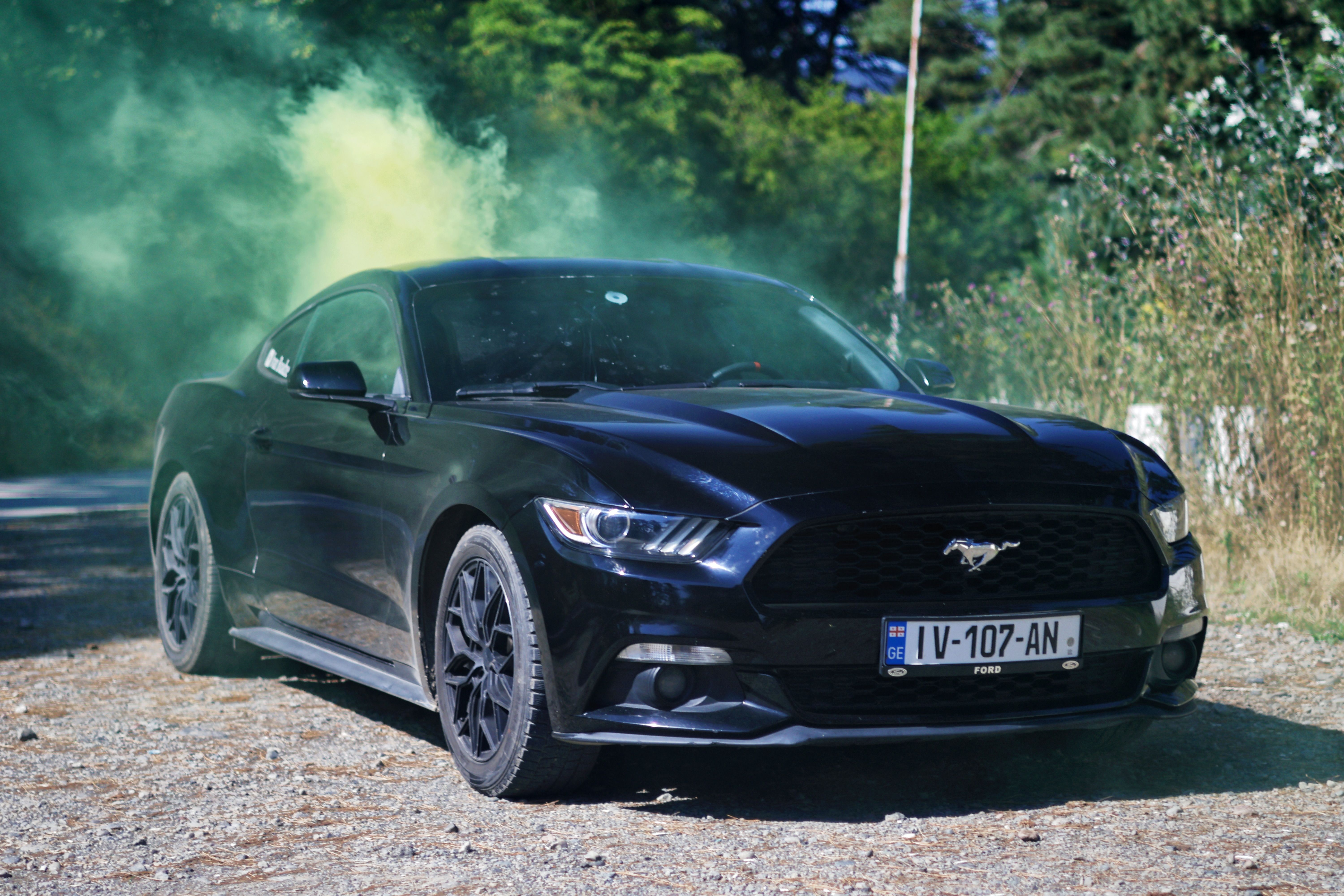 A sleek black sports car outdoors surrounded by vibrant green smoke clouds.