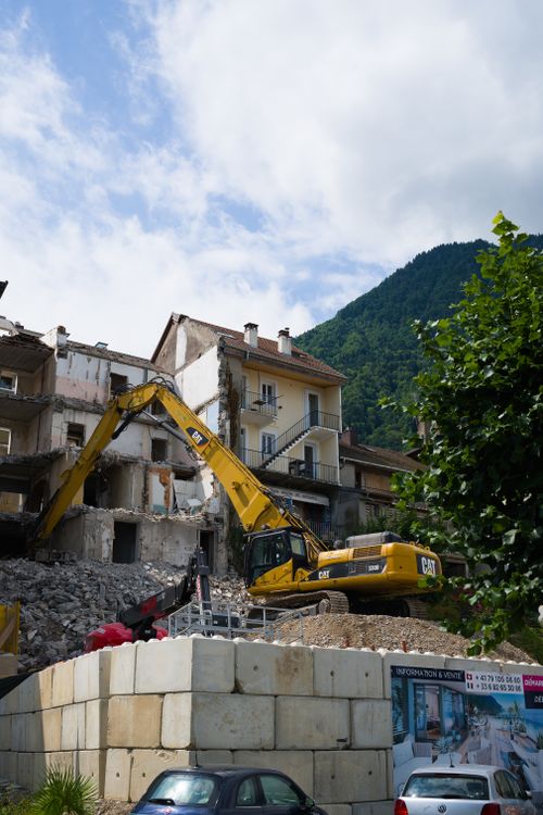 Free Excavator demolishing building in a European village with mountain scenery. Stock Photo
