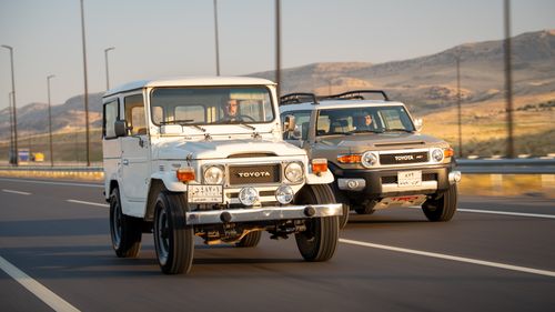 Free Vintage and modern Toyota SUVs drive side by side on a scenic highway during the day. Stock Photo