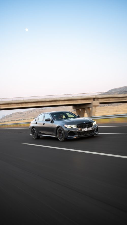 Free Shiny black car speeds on a highway with a bridge in the background at twilight. Stock Photo