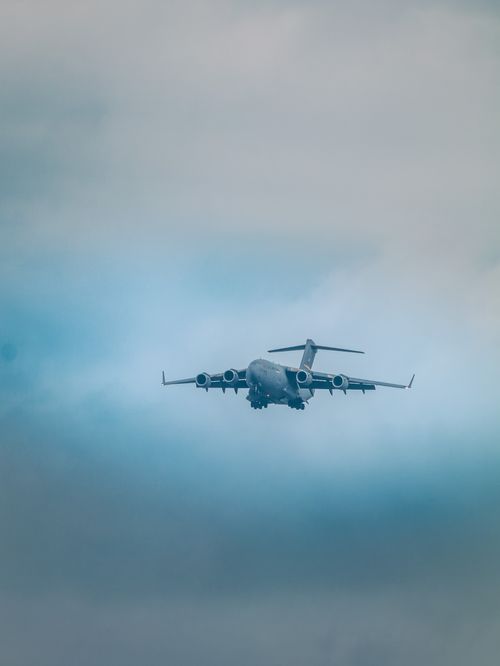 Free C-17 Globemaster flying through overcast skies, creating a dramatic aviation scene. Stock Photo