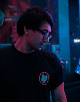 Stylish young man with glasses in a moody, neon-lit environment.