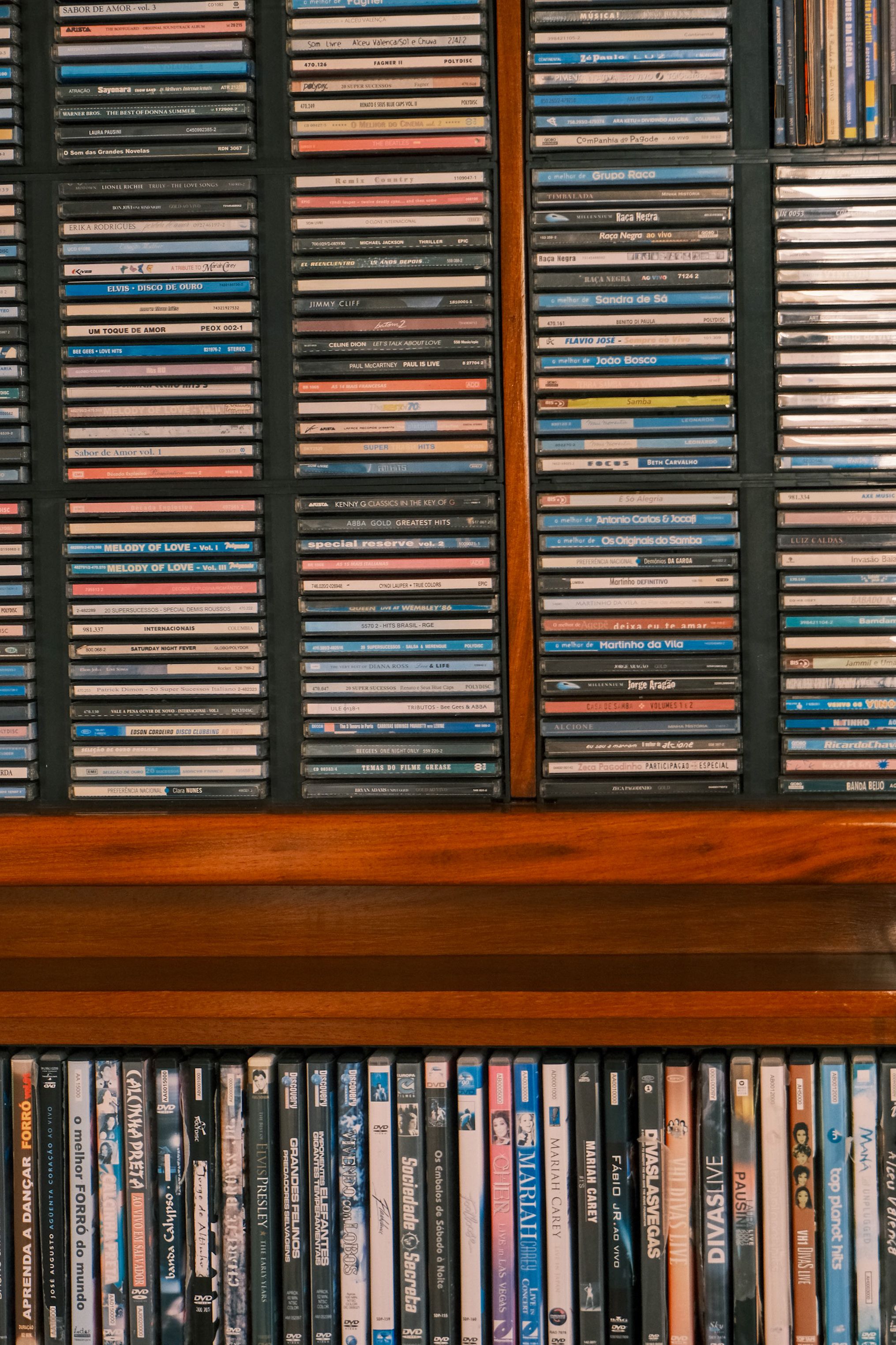 A detailed view of organized vintage CDs and DVDs in a wooden shelf, capturing nostalgia and music collection culture.