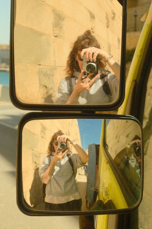 Free Artistic reflection of a person holding a vintage camera, captured in car mirrors outdoors. Stock Photo