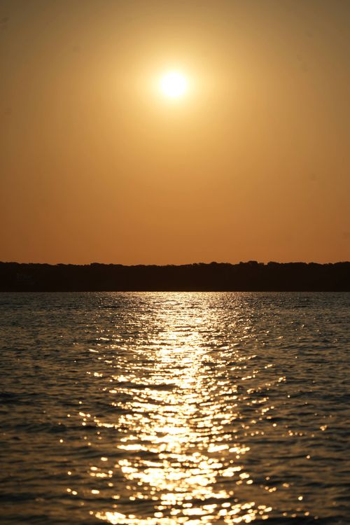 Free Beautiful sunset over calm lake reflecting a warm golden glow in the evening. Stock Photo
