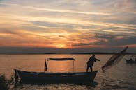 Silhouette Of Man Standing On Boat During Sunset
