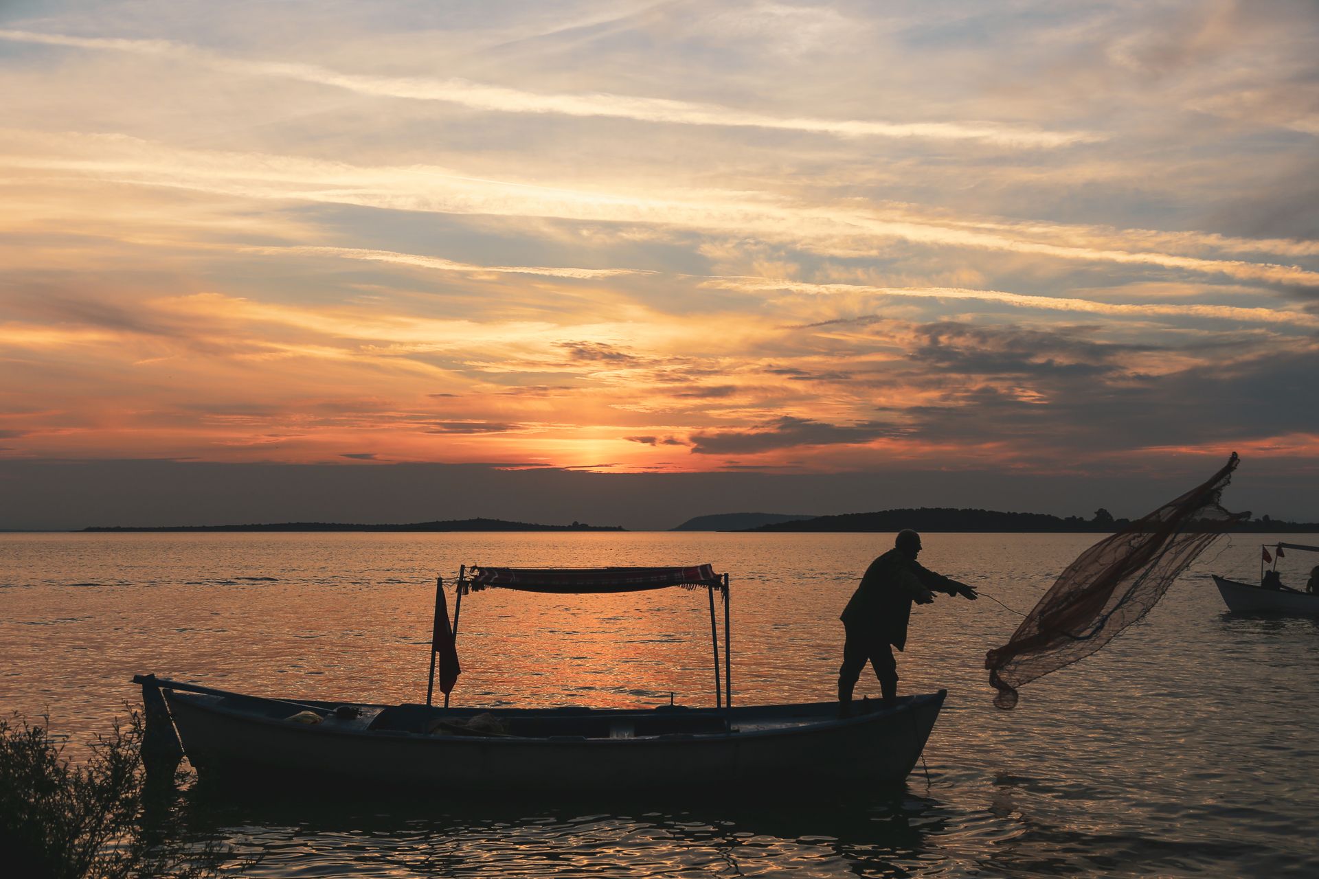 Silhouette of a fisherman casting a net from a boat during a stunning sunset in Gölyazı, Turkey.