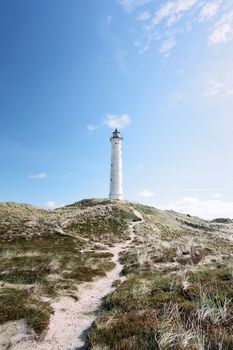 Hvide Sande lighthouse standing tall on sandy dunes, under a clear blue sky in Denmark.
