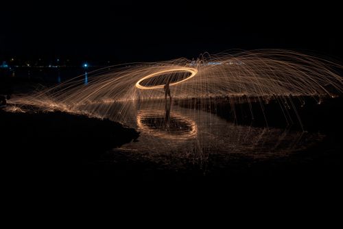 Free Captivating steel wool light painting at night with dynamic sparks and reflections by the beach. Stock Photo