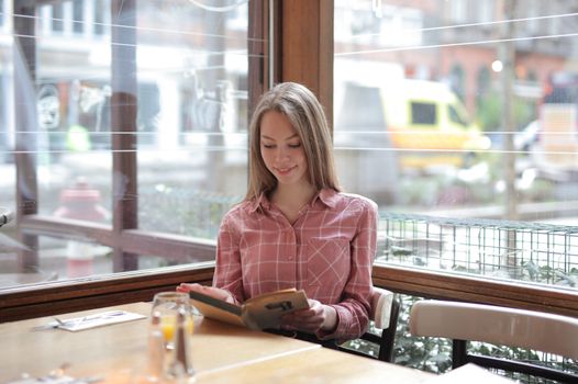 A woman enjoys reading a book while sitting at a cafe table with a glass of orange juice.. pexels, woman, enjoys
