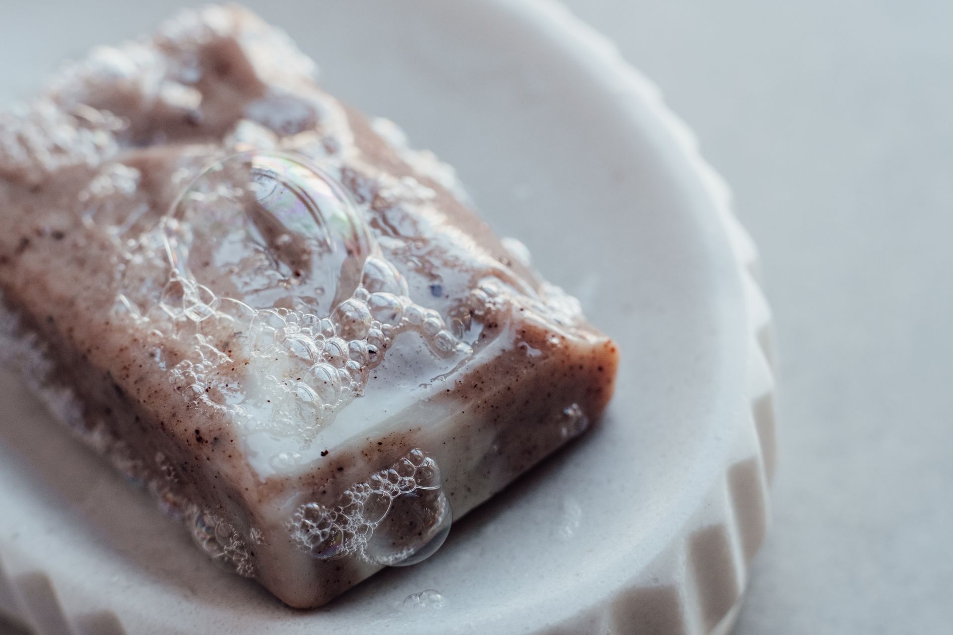 Detailed close-up of a handmade organic soap bar with bubbles on a dish, highlighting its texture.
