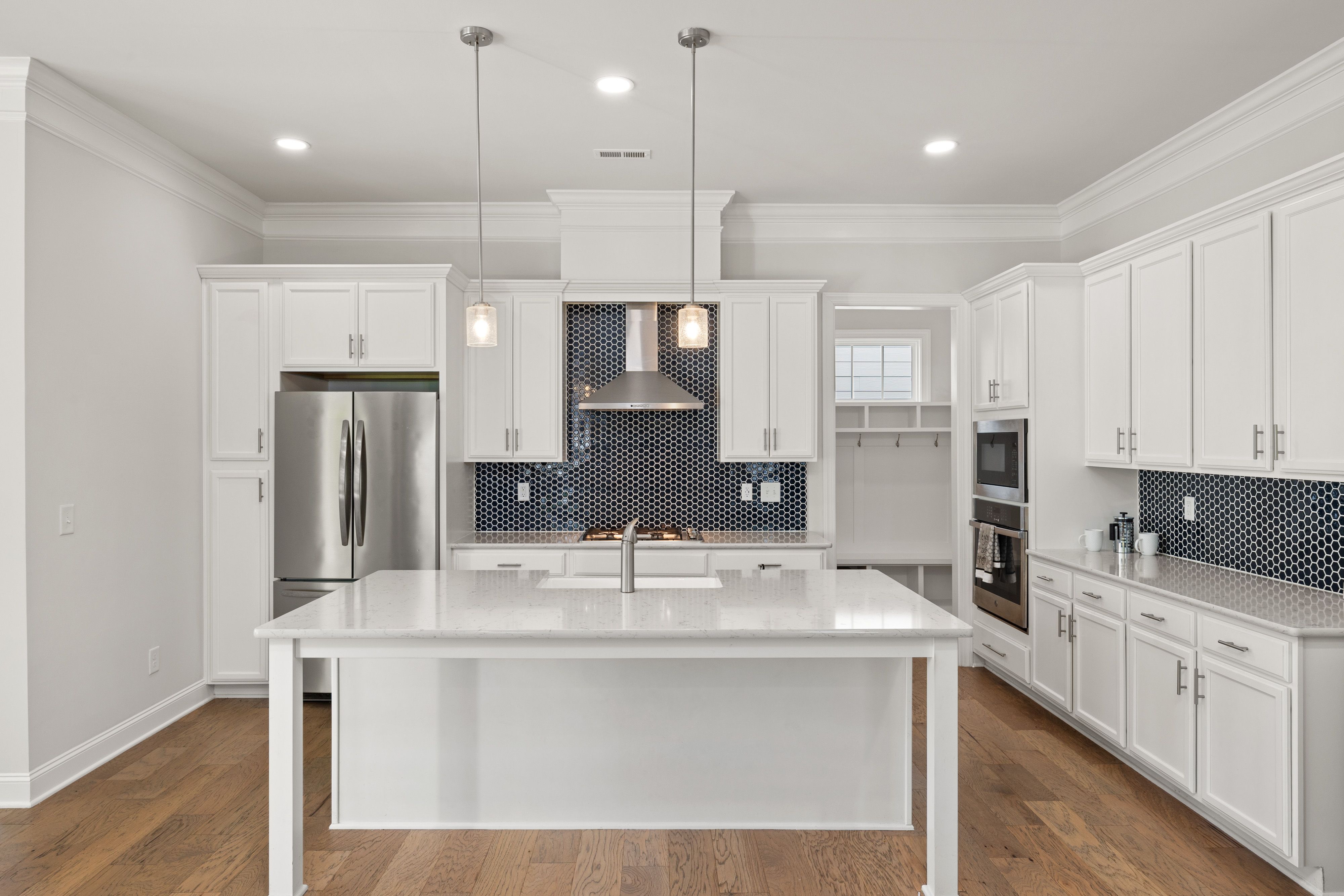 Bright white modern kitchen with island, stainless steel appliances, and black patterned backsplash