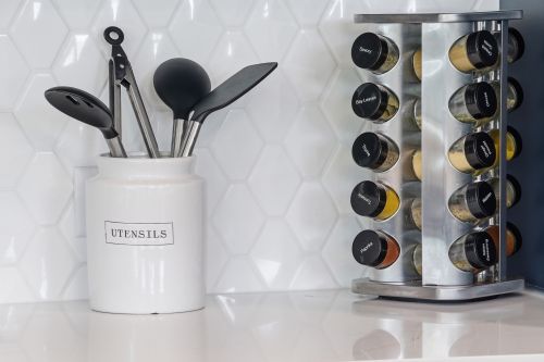 Free A sleek kitchen setup featuring utensils in a jar and a rotating spice rack on a white countertop. Stock Photo
