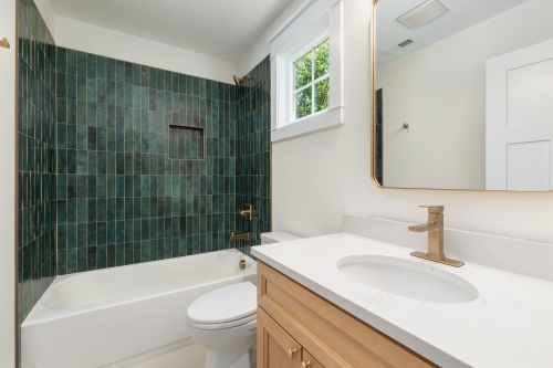 Free Elegant bathroom featuring a green tiled wall, white tub, and wooden vanity with gold fixtures, offering a modern and stylish look. Stock Photo