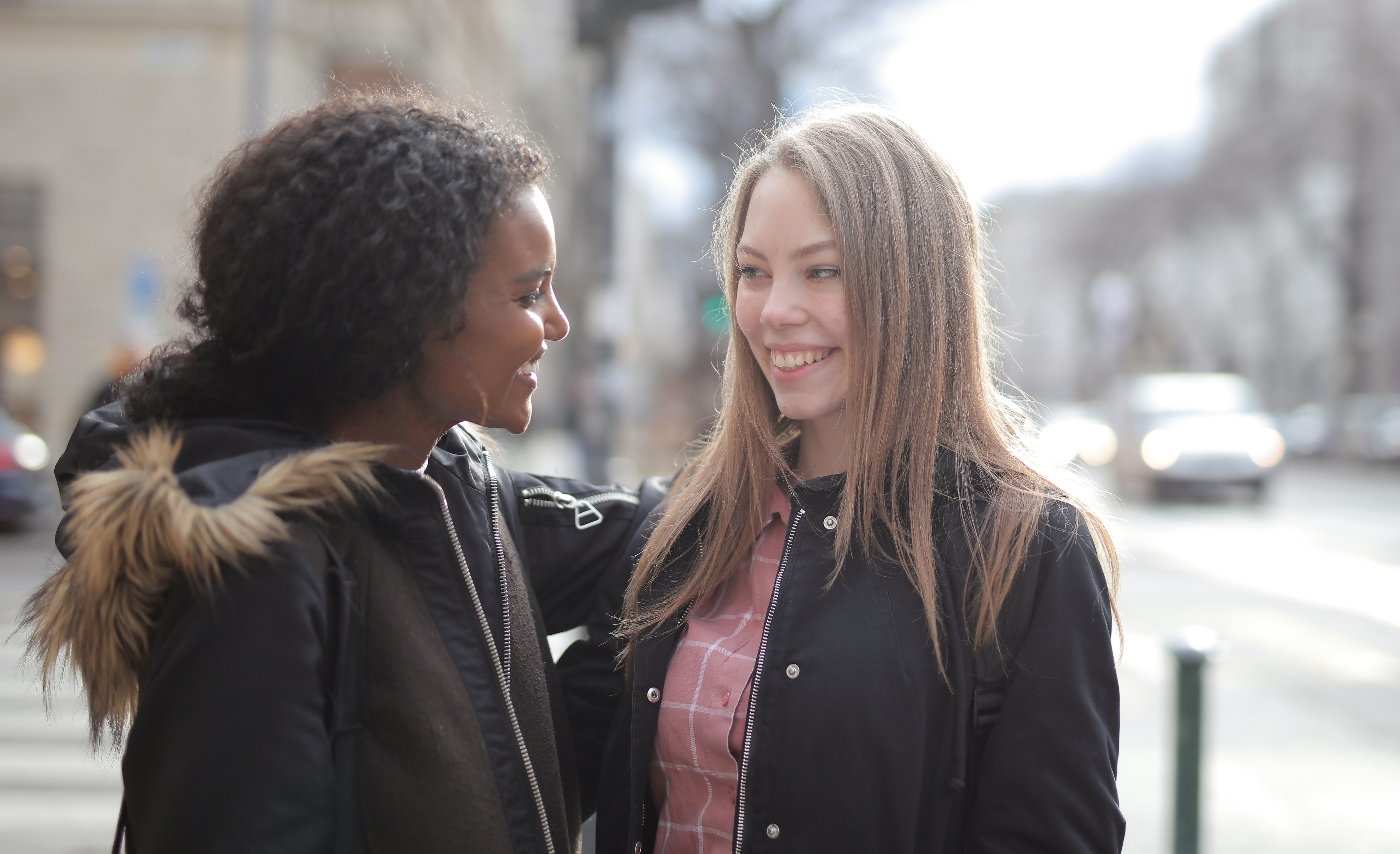Two women in winter jackets happily interact outdoors, showcasing friendship and warmth.