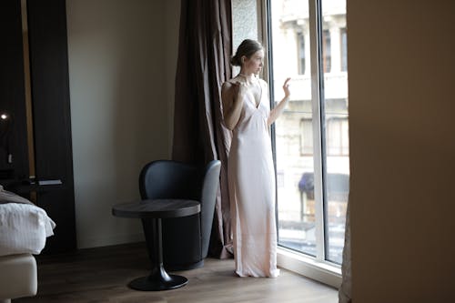 Woman in White Dress Standing Near Window