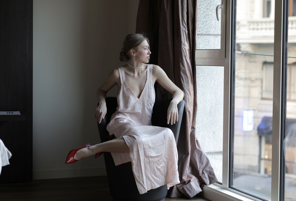 A woman in a white spaghetti-strap slip dress by a window