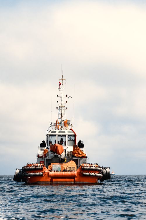 Free A bright orange tugboat sails through the Pacific Ocean near Lima, Peru under a cloudy sky. Stock Photo