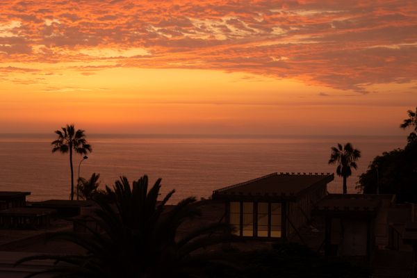 Uma vista deslumbrante do pôr do sol sobre o Oceano Pacífico em Callao, Lima, com palmeiras em silhueta.
