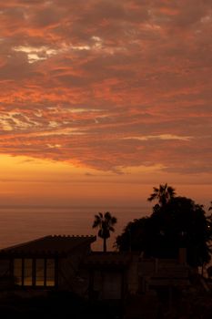 Stunning sunset view over Lima's coastline with vibrant orange clouds and silhouettes of palm trees.