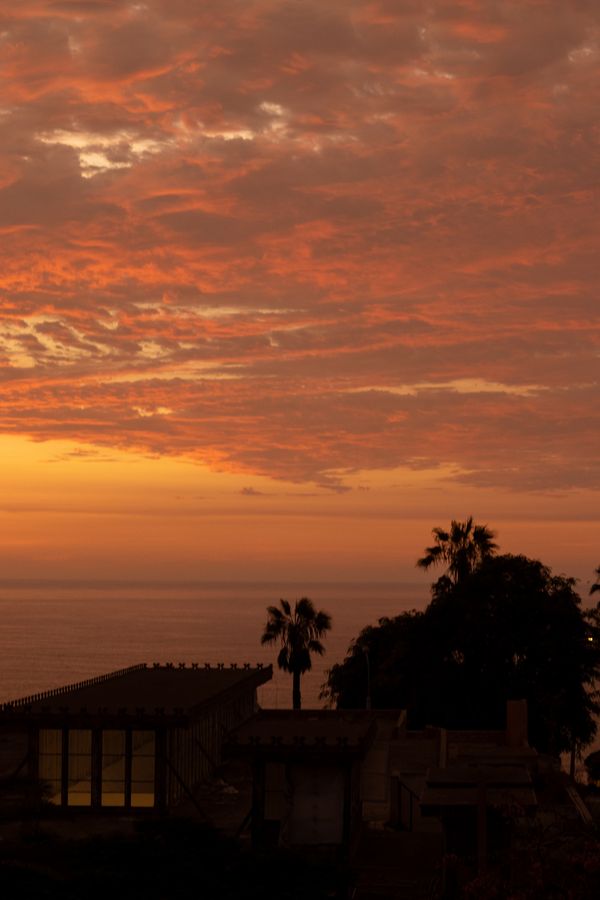 Vista deslumbrante do pôr do sol sobre a costa de Lima, com nuvens laranja vibrantes e silhuetas de palmeiras.