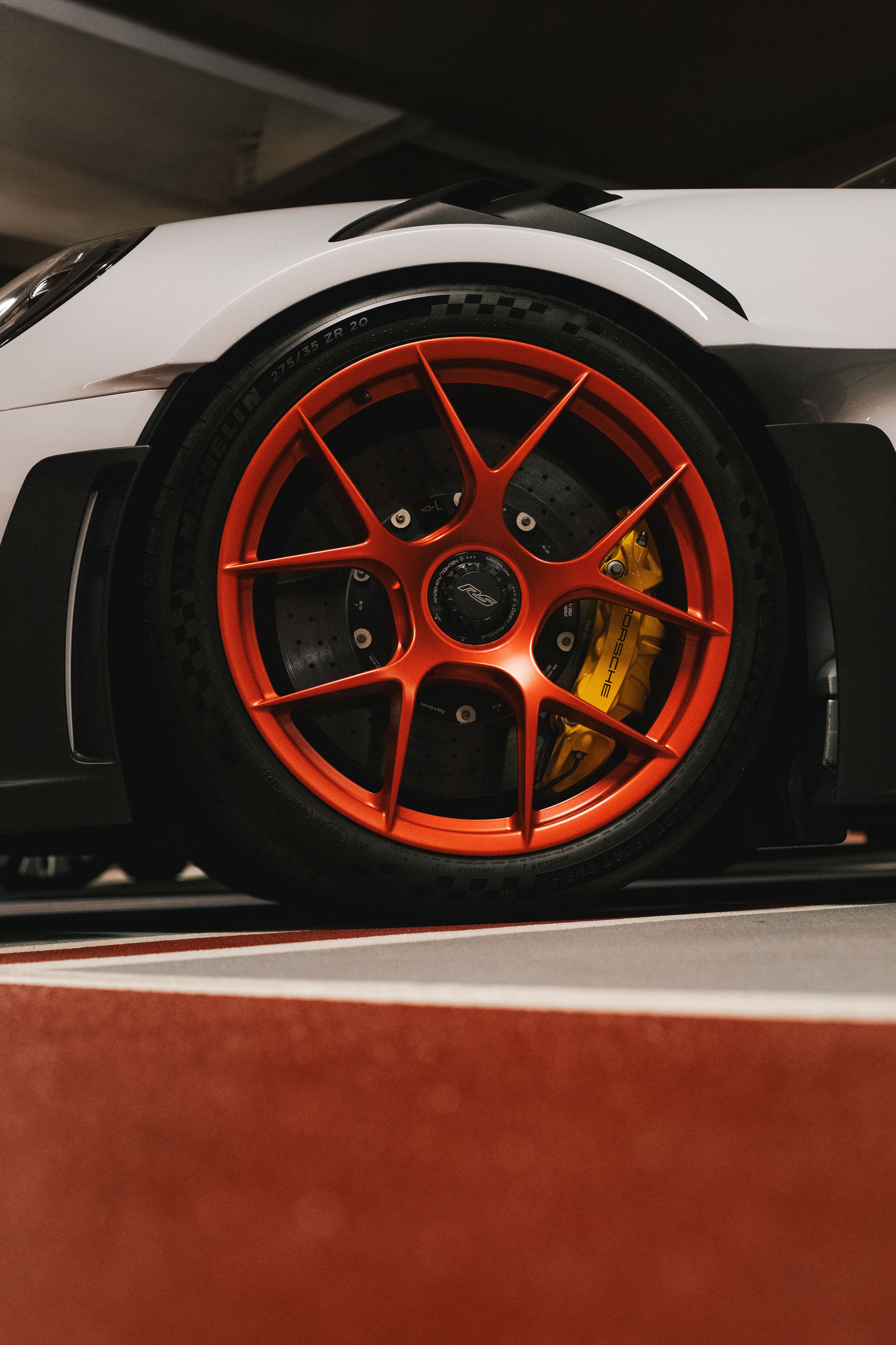 Detailed shot of a Porsche wheel with orange rim and yellow caliper.