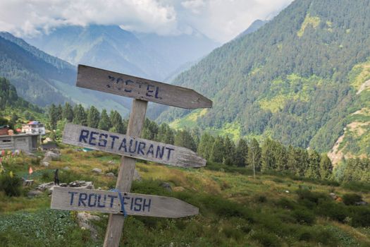 Wooden signpost directing to hostel, restaurant, and trout fishing in a scenic mountain setting.