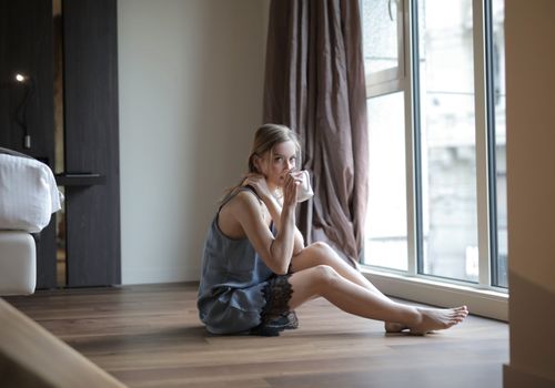 Relaxing scene of a woman sipping coffee by a window in a cozy home setting.