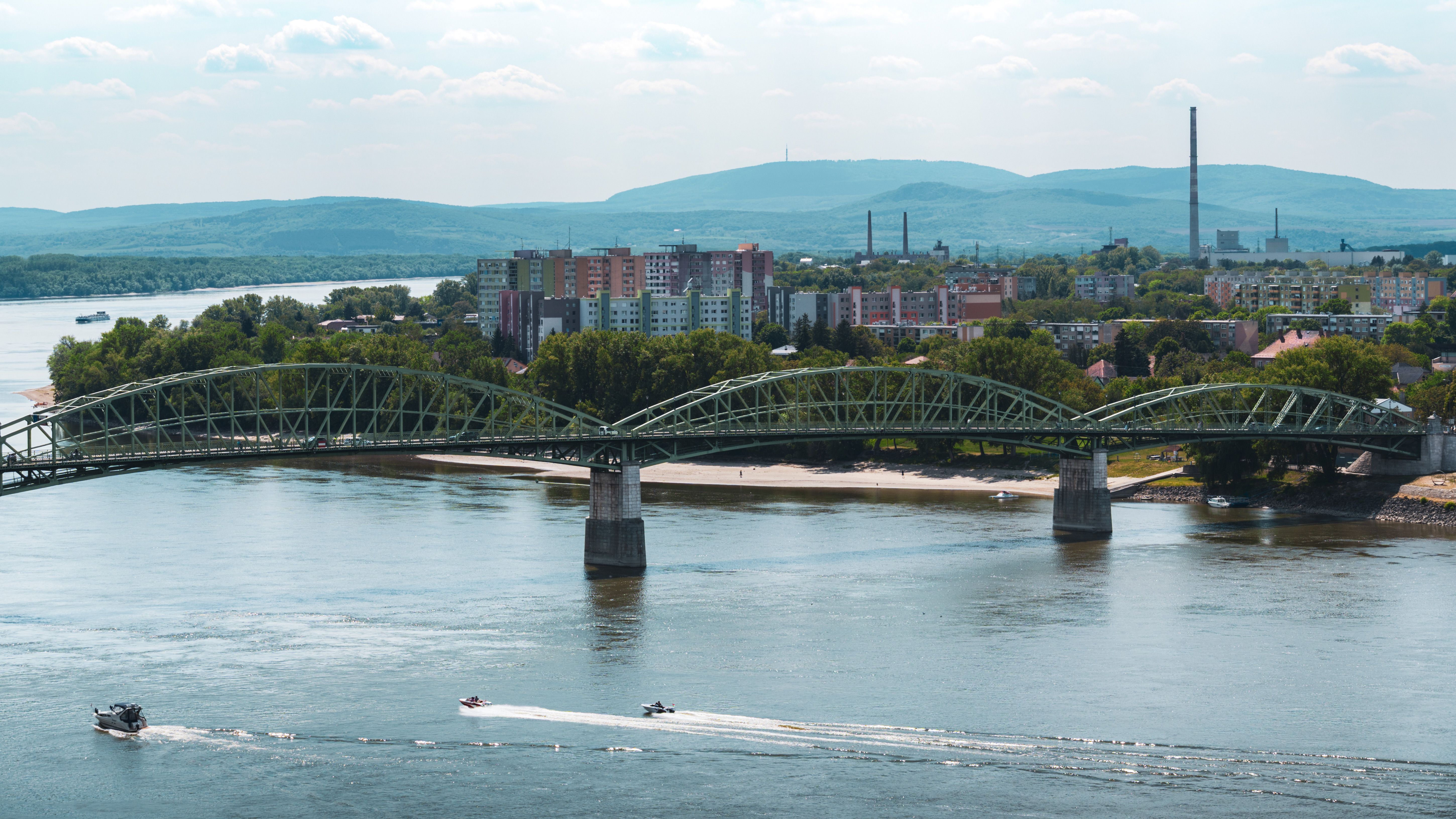 Bridge spanning Danube River in Esztergom, Hungary with cityscape and boats.