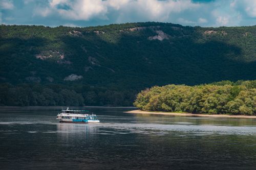 Free A scenic view of a boat cruising on the Danube River with lush hills and forested banks in Hungary. Stock Photo