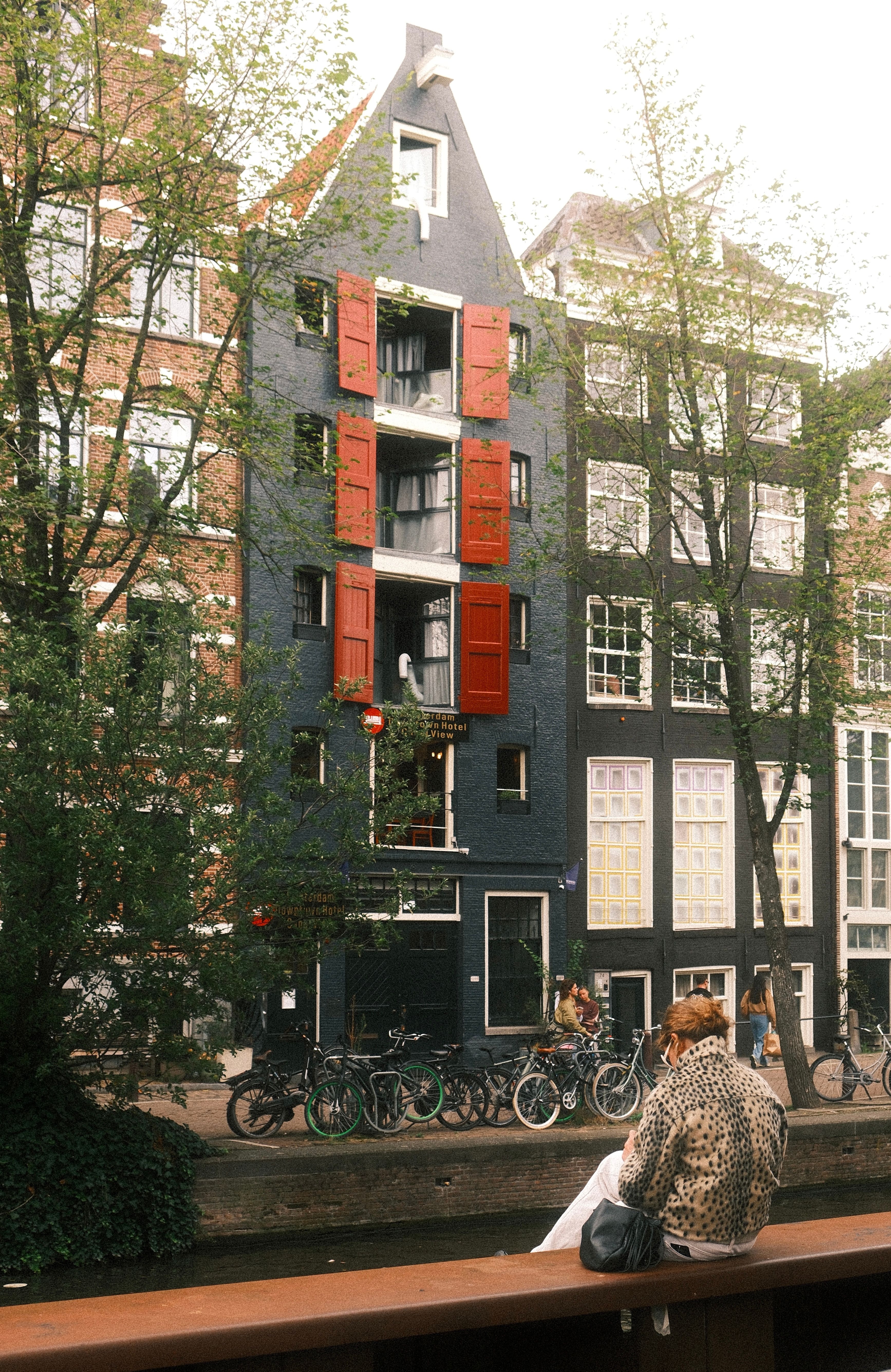Scenic view of traditional Dutch architecture along an Amsterdam canal with a woman sitting by the water.