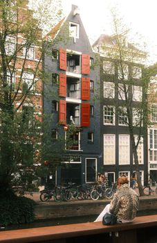 Scenic view of traditional Dutch architecture along an Amsterdam canal with a woman sitting by the water.