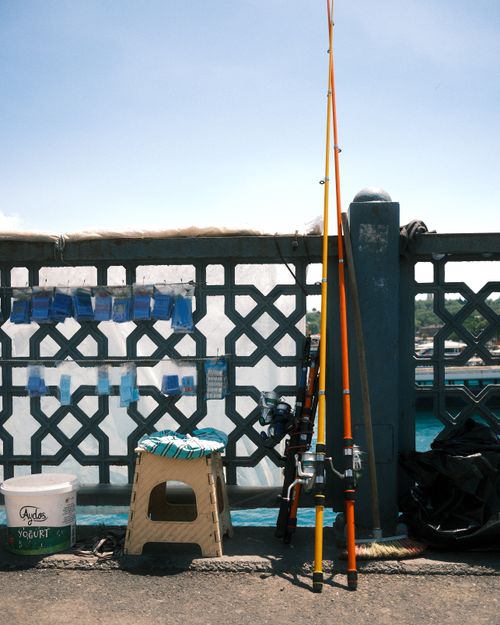 Free A fishing setup on a bridge with rods, chair, and bucket on a bright sunny day, offering an outdoor fishing vibe. Stock Photo