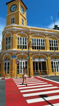 Vibrant yellow Sino-Portuguese building with clock tower in Phuket, Thailand under clear blue skies.