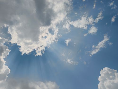 Free Captivating view of sun rays piercing through fluffy clouds in a bright blue sky. Stock Photo