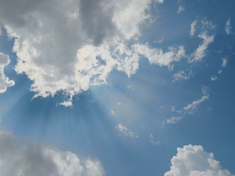 Beautiful sun rays streaming through fluffy clouds in a clear blue sky, captured in Silchar, India.