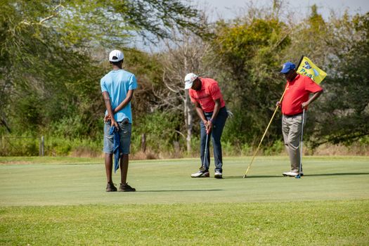 Three men enjoying a game of golf on a sunny day at a course in Manzini, Eswatini.